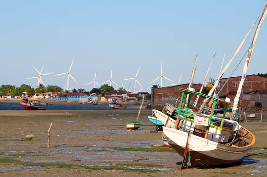 Em maré baixa barcos ficam encalhados. Ao fundo, novo parque eólico da Petrobrás.