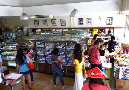 O interior da padaria com grande variedade de pães, salgados e doces.  Até tem "poló páu".